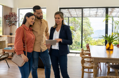 Real estate agent using a digital tablet to show pictures of a house to a couple at a showing.