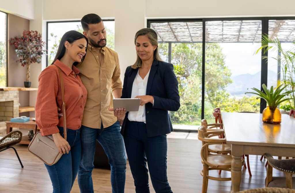 Real estate agent using a digital tablet to show pictures of a house to a couple at a showing.